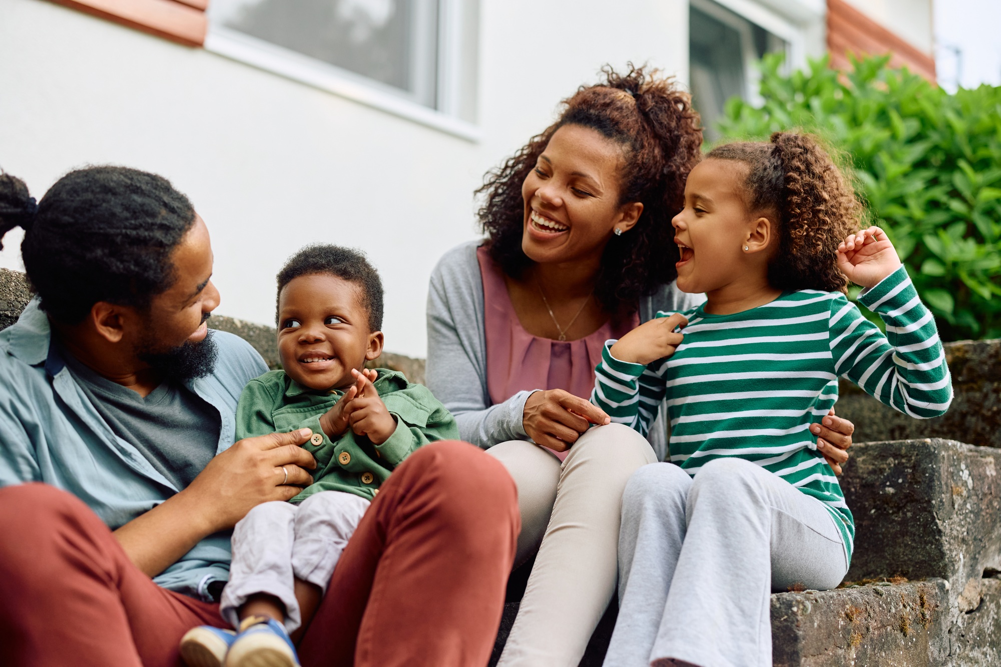 Happy black family talking while relaxing on staircase in front of their house.